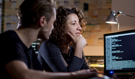 Two developers look at a computer monitor with code